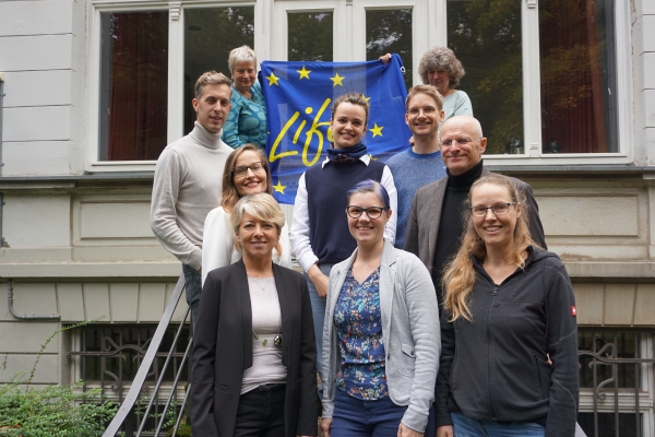Gruppenfoto mit EU-blauer Flagge mit der Aufschrift "Life", außenherum gelbe Sterne